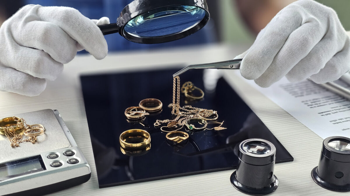 Expert evaluates various gold jewelry pieces with magnifying glass and tweezers in a bright workspace