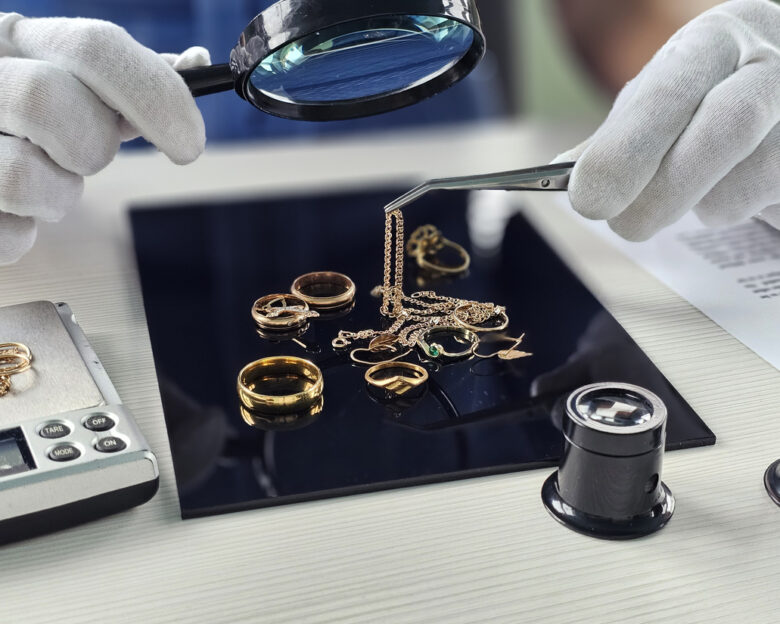 Expert evaluates various gold jewelry pieces with magnifying glass and tweezers in a bright workspace
