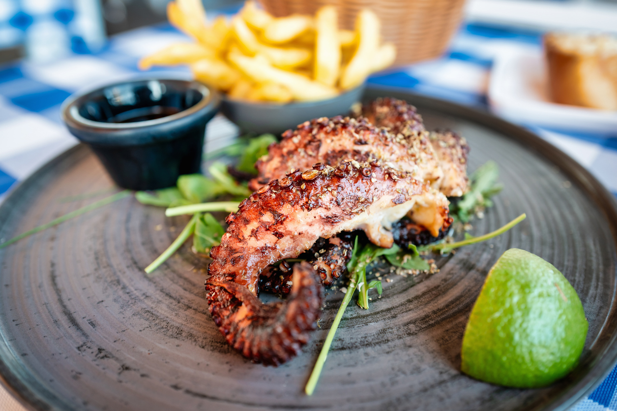 Greece Grilled Octopus Tentacle seasoned with Herbs and Spices, served with Arugula Salad, Lime and French Fries. Cyprus Island, Greece, Southern Europe