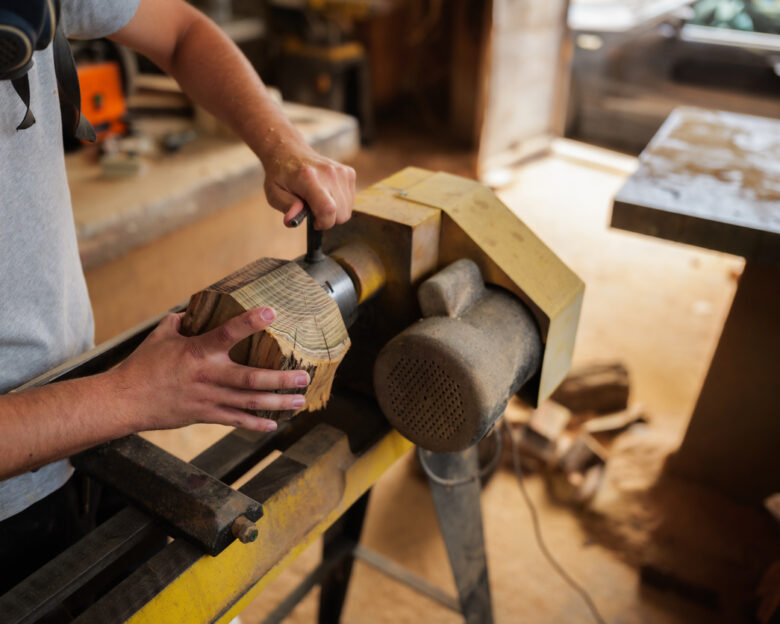 Carpenter wearing a protective mask, skillfully working wood on a lathe in an old, dusty workshop, meticulously crafting a unique handmade piece of furniture with precision and care