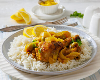 close-up of Chicken Yassa stewed in mustard, served with caramelized onions, olives, and basmati rice on a white plate on white wood table,close-up, not AI generated