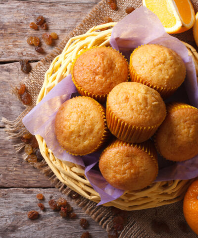 Citrus muffins in a basket and fresh oranges on an old table close-up. horizontal view from above