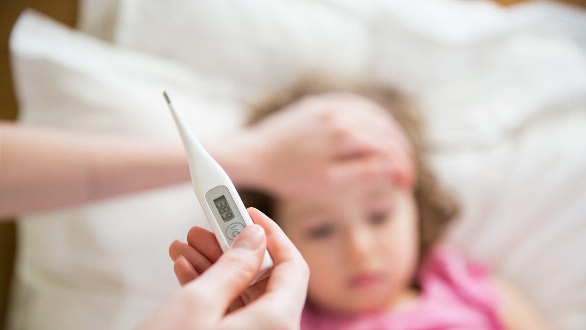 Close-up thermometer. Mother measuring temperature of her ill kid. Sick child with high fever laying in bed and mother holding thermometer. Hand on forehead.