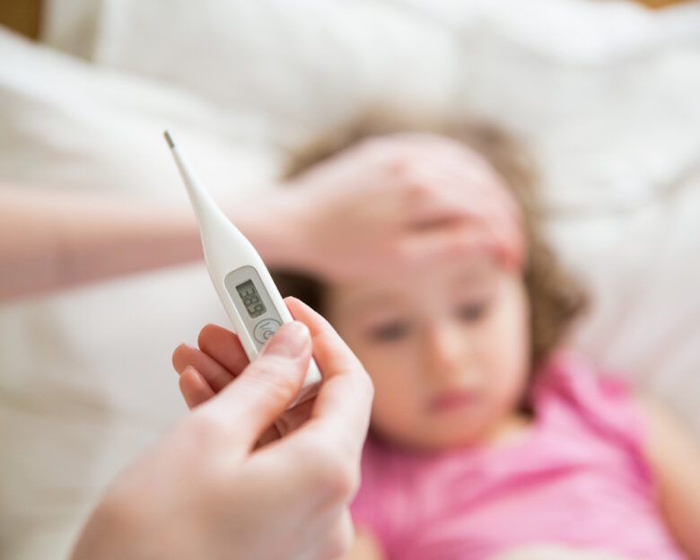 Close-up thermometer. Mother measuring temperature of her ill kid. Sick child with high fever laying in bed and mother holding thermometer. Hand on forehead.