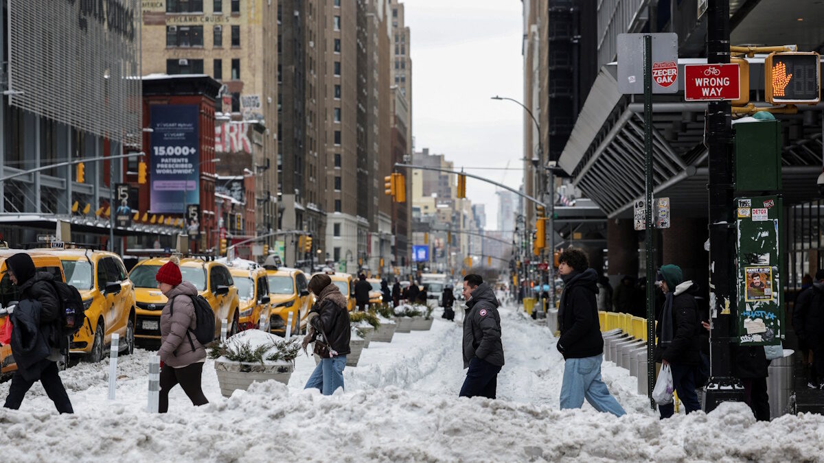 Πεζοί περπατούν σε έναν χιονισμένο δρόμο, καθώς μια μεγάλη χειμερινή καταιγίδα εξαπλώνεται στη Νέα Υόρκη