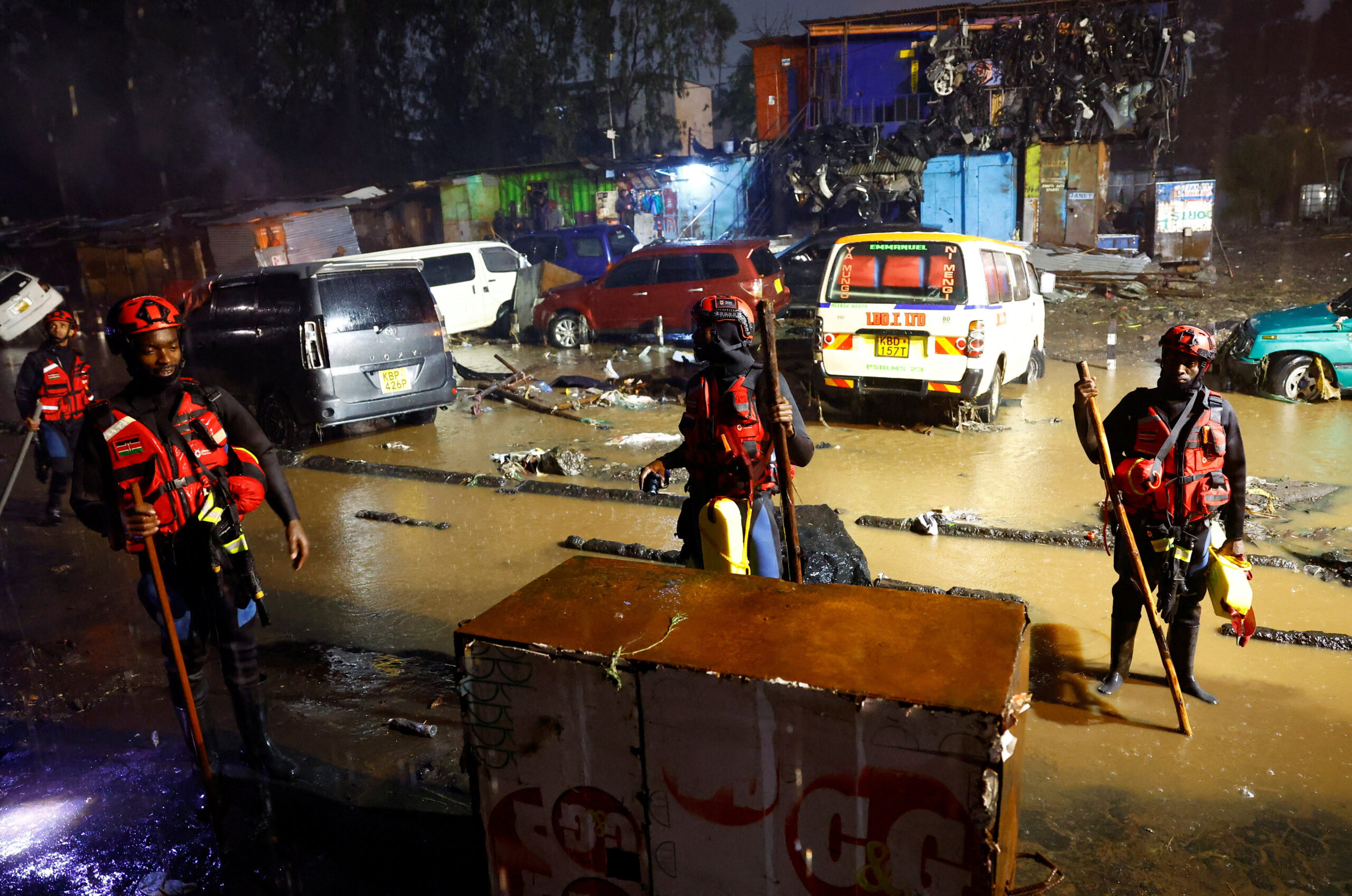 People stand near a trench polluted with petroleum waste from the wreckages of vehicles destroyed following heavy rainfall in the Grogan area, popular for automotive workshops and secondhand spare parts, in downtown Nairobi, Kenya, March 7, 2026. REUTERS/Thomas Mukoya       TPX IMAGES OF THE DAY