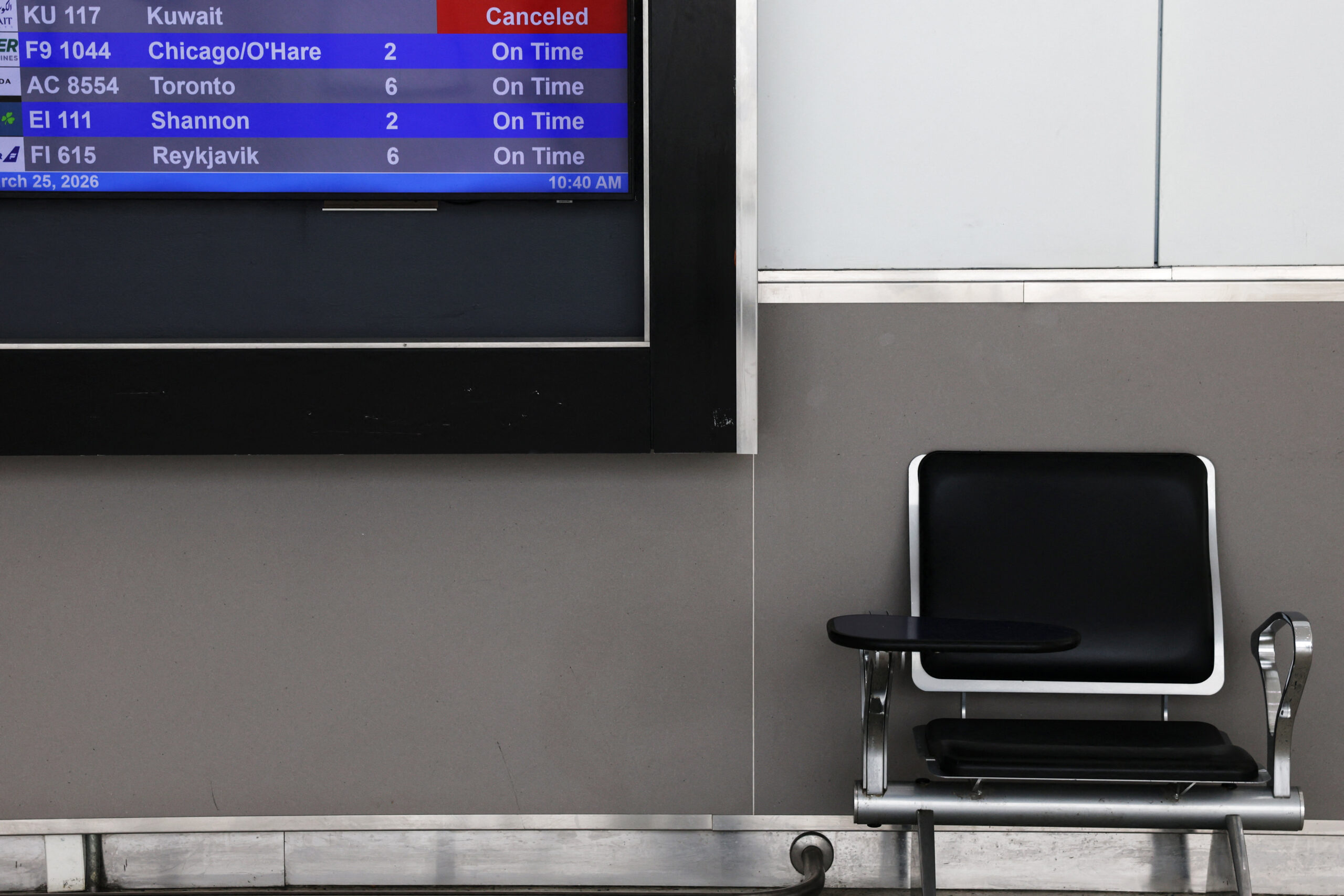 Μια άδεια καρέκλα δίπλα σε πίνακα αναχωρήσεων, όπου εμφανίζεται μια ακυρωμένη πτήση της Kuwait Airways