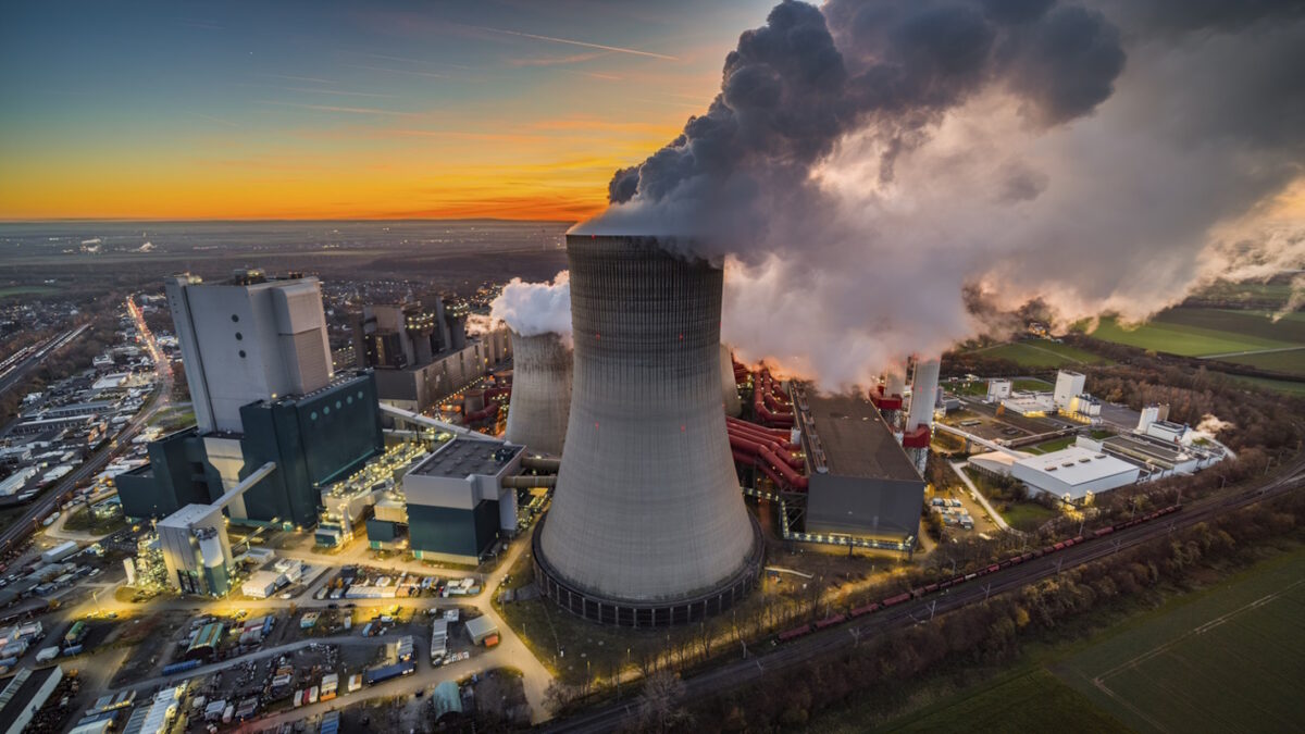 Aerial view of a large cooling tower releasing steam at an industrial power plant during sunset. Dramatic evening light and rising vapor highlight large-scale electricity generation, heavy industrial infrastructure, and energy production facilities.