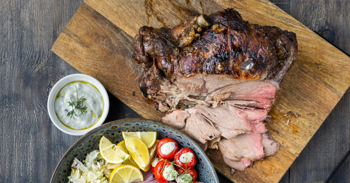 Spit roast lamb, salad and sauce on wood chopping board.