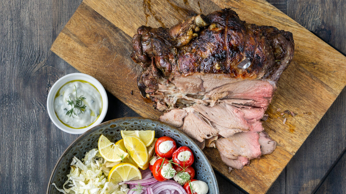 Spit roast lamb, salad and sauce on wood chopping board.