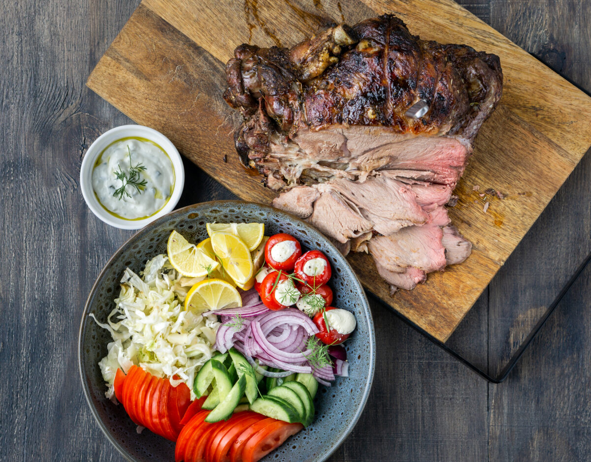 Spit roast lamb, salad and sauce on wood chopping board.
