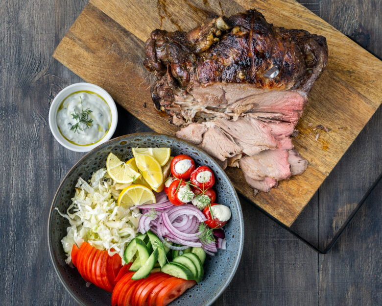 Spit roast lamb, salad and sauce on wood chopping board.