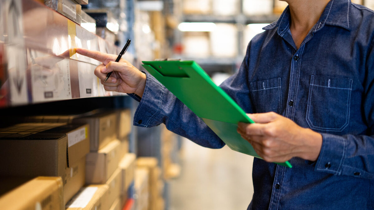 Manager man worker doing stocktaking of product management in cardboard box on shelves in warehouse. Physical inventory count."n Male professional assistant checking stock in factory.
