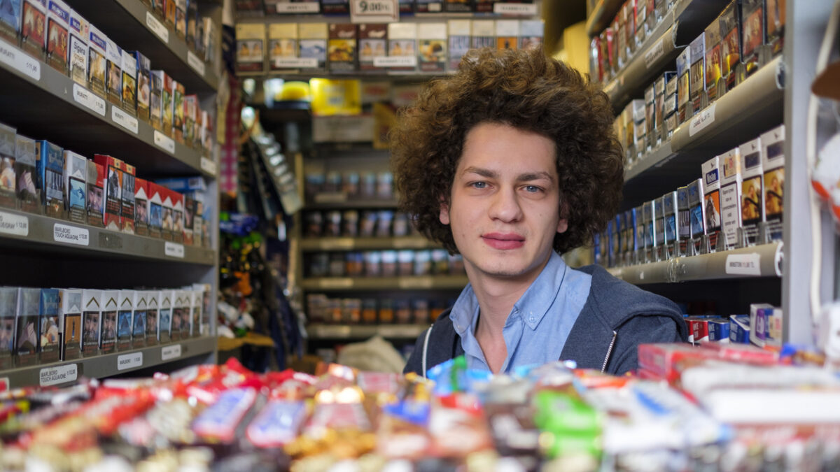 A young salesman in a tobacco kiosk selling numerous kinds of cigars, cigarettes, and tobacco products. His kiosk is located on Istiklal Avenue in the heart of Istanbul city, a real smoker's heaven with vibrant cigarette packs in the neighborhood