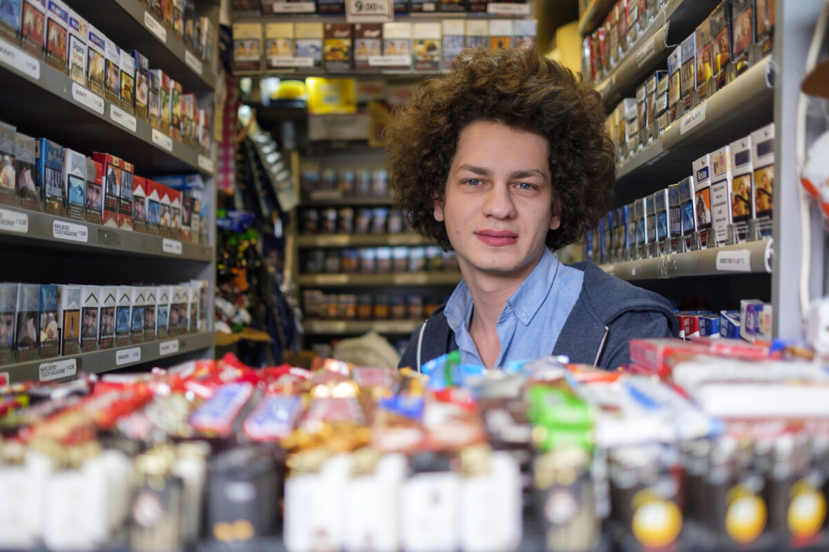 A young salesman in a tobacco kiosk selling numerous kinds of cigars, cigarettes, and tobacco products. His kiosk is located on Istiklal Avenue in the heart of Istanbul city, a real smoker's heaven with vibrant cigarette packs in the neighborhood