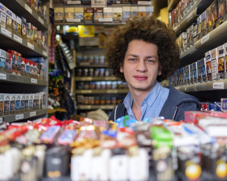 A young salesman in a tobacco kiosk selling numerous kinds of cigars, cigarettes, and tobacco products. His kiosk is located on Istiklal Avenue in the heart of Istanbul city, a real smoker's heaven with vibrant cigarette packs in the neighborhood