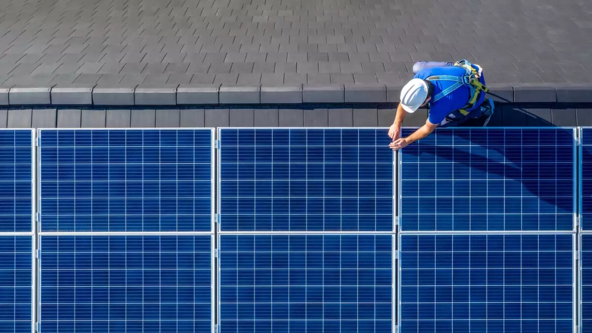Male engineer in blue suit and protective helmet installing photovoltaic panel system. Professional electrician mounting solar module on roof. Alternative energy ecological concept