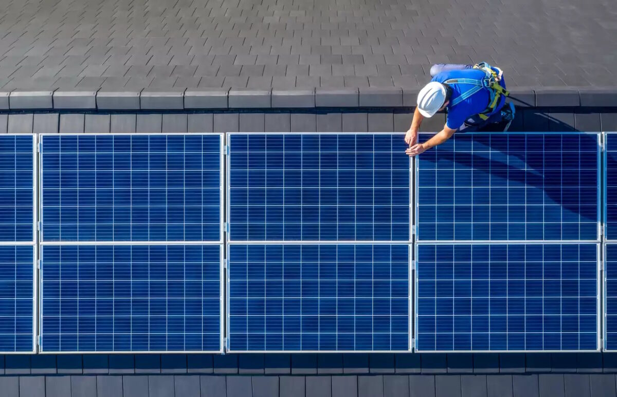 Male engineer in blue suit and protective helmet installing photovoltaic panel system. Professional electrician mounting solar module on roof. Alternative energy ecological concept