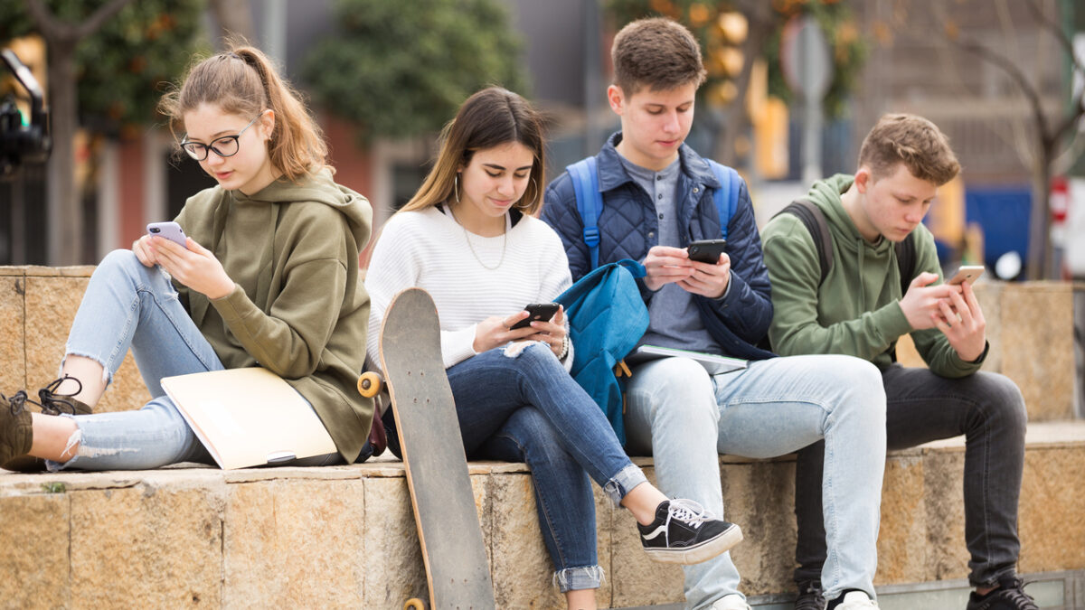 Four teenagers chatting on their smartphone on walking