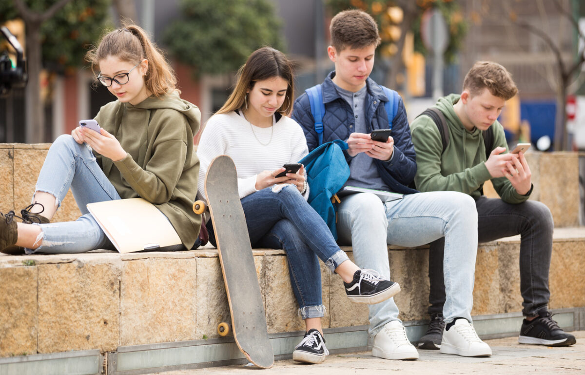 Four teenagers chatting on their smartphone on walking