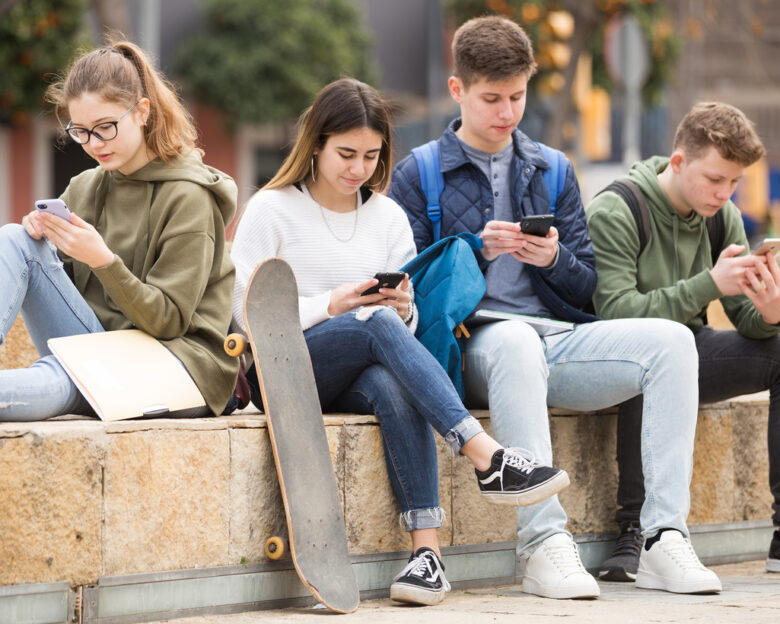 Four teenagers chatting on their smartphone on walking