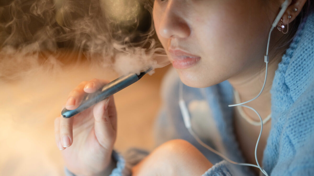 Young woman vaping an electronic cigarette for relax while working at night