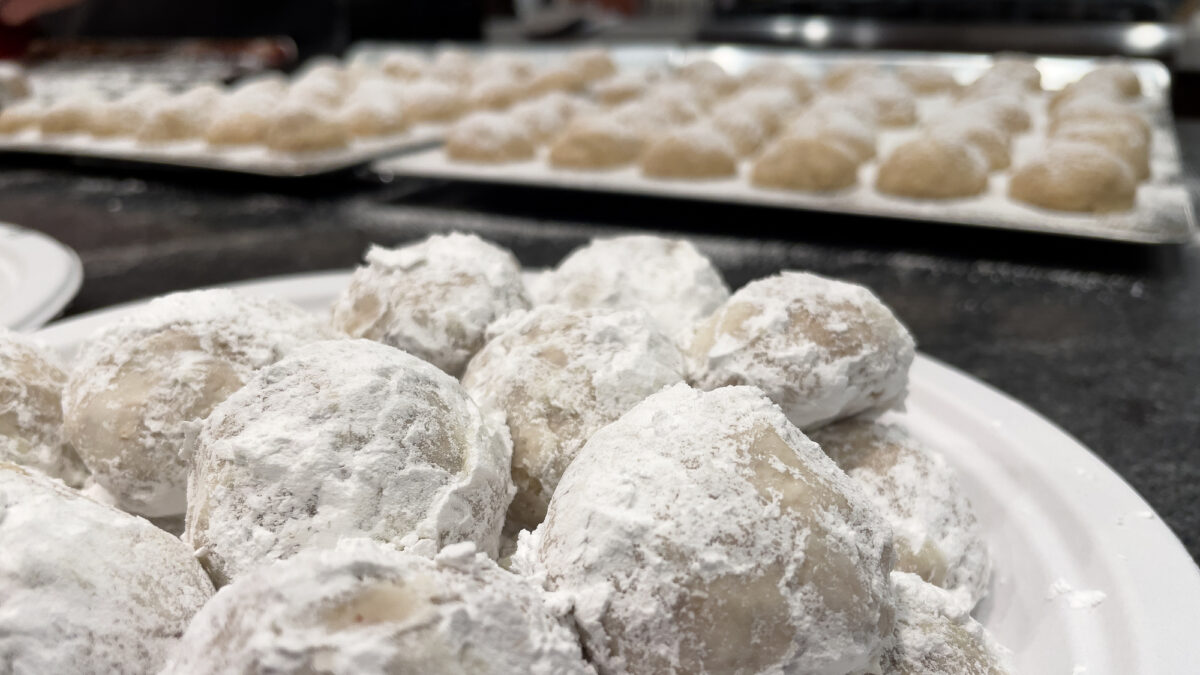 Close-up of white snowball cookies covered with powdered sugar on a plate. Cookie sheet with more snowball Christmas cookies in the background. Baking Christmas cookies