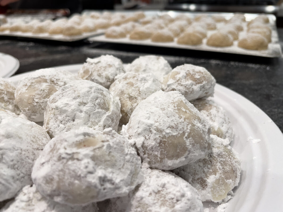 Close-up of white snowball cookies covered with powdered sugar on a plate. Cookie sheet with more snowball Christmas cookies in the background. Baking Christmas cookies