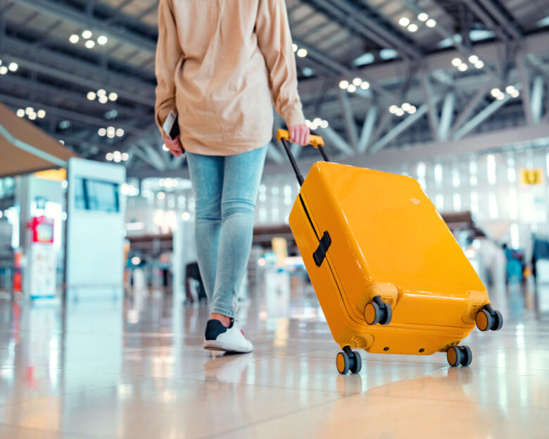 Young female traveler passenger walking with a yellow suitcase at the modern Airport Terminal, Back view of woman on her way to flight boarding gate, Ready for travel or vacation journey