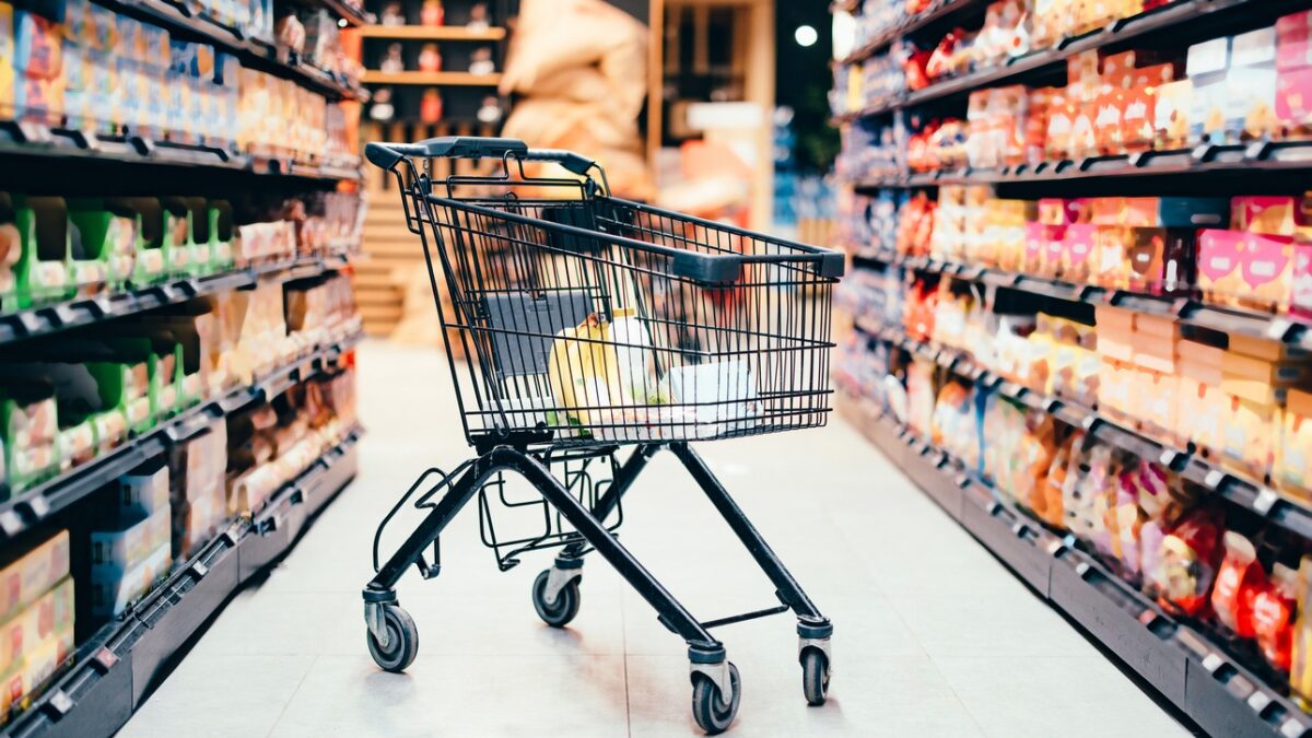 Abandoned shopping cart with groceries in the middle of the aisle in the supermarket. No one is on the photo.