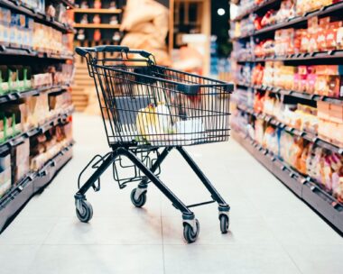 Abandoned shopping cart with groceries in the middle of the aisle in the supermarket. No one is on the photo.