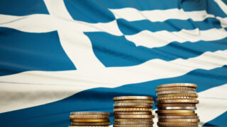 Rising stack of coins with Greek flag in the background. Economy, finance, interest rates concept.