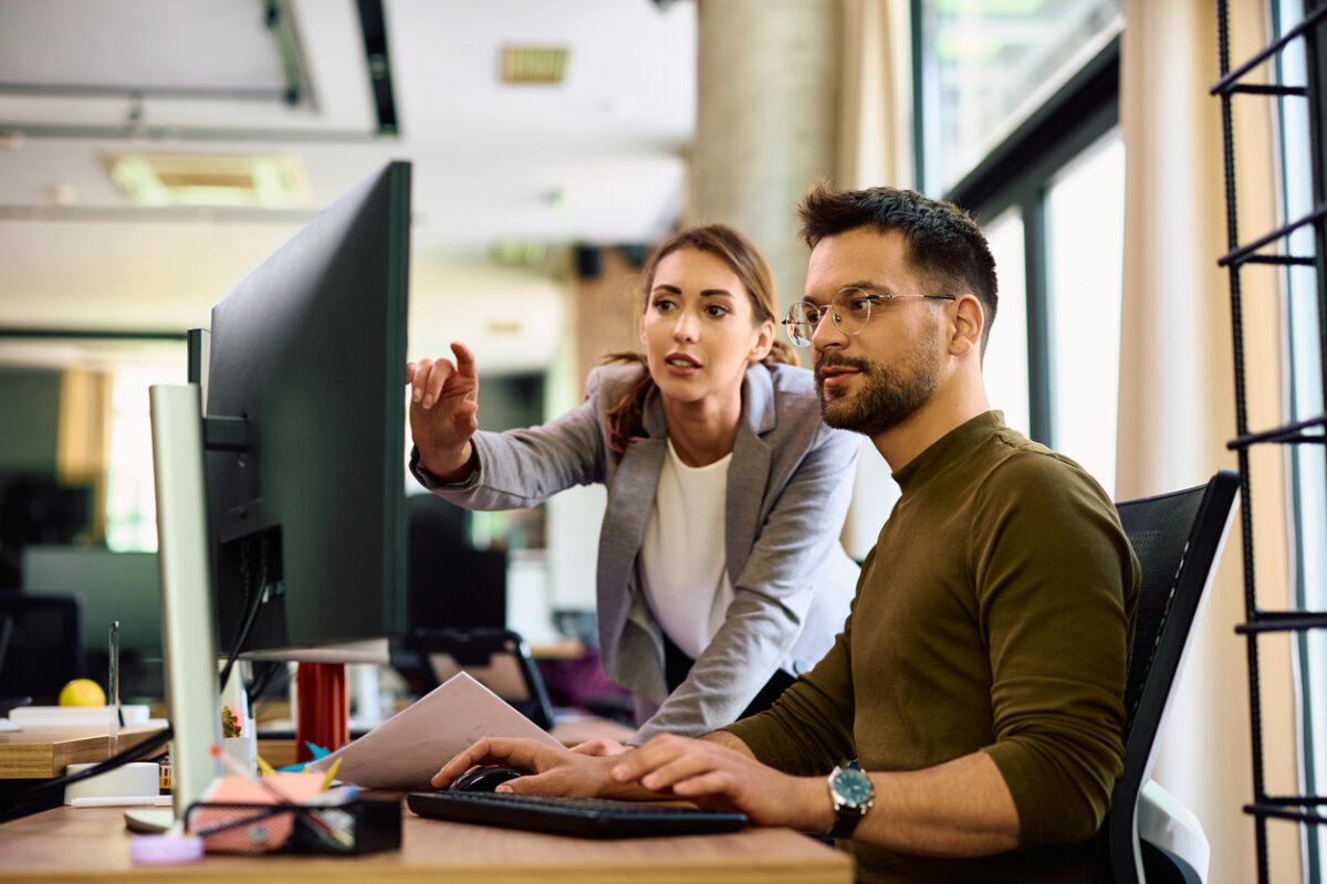Young entrepreneur and his female coworker using desktop PC while working in the office