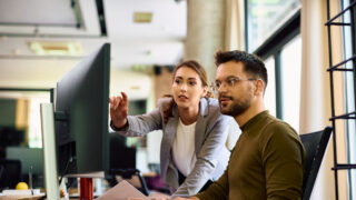 Young entrepreneur and his female coworker using desktop PC while working in the office