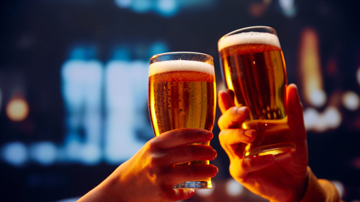 Hands holding lager light foamy big beer glasses and clinking. Two friends sitting in bar and drinking alcohol drinks. Concept of Beer Fest, party, celebration, taste, national traditions.
