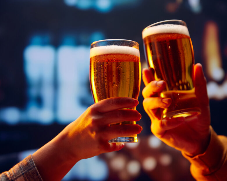 Hands holding lager light foamy big beer glasses and clinking. Two friends sitting in bar and drinking alcohol drinks. Concept of Beer Fest, party, celebration, taste, national traditions.