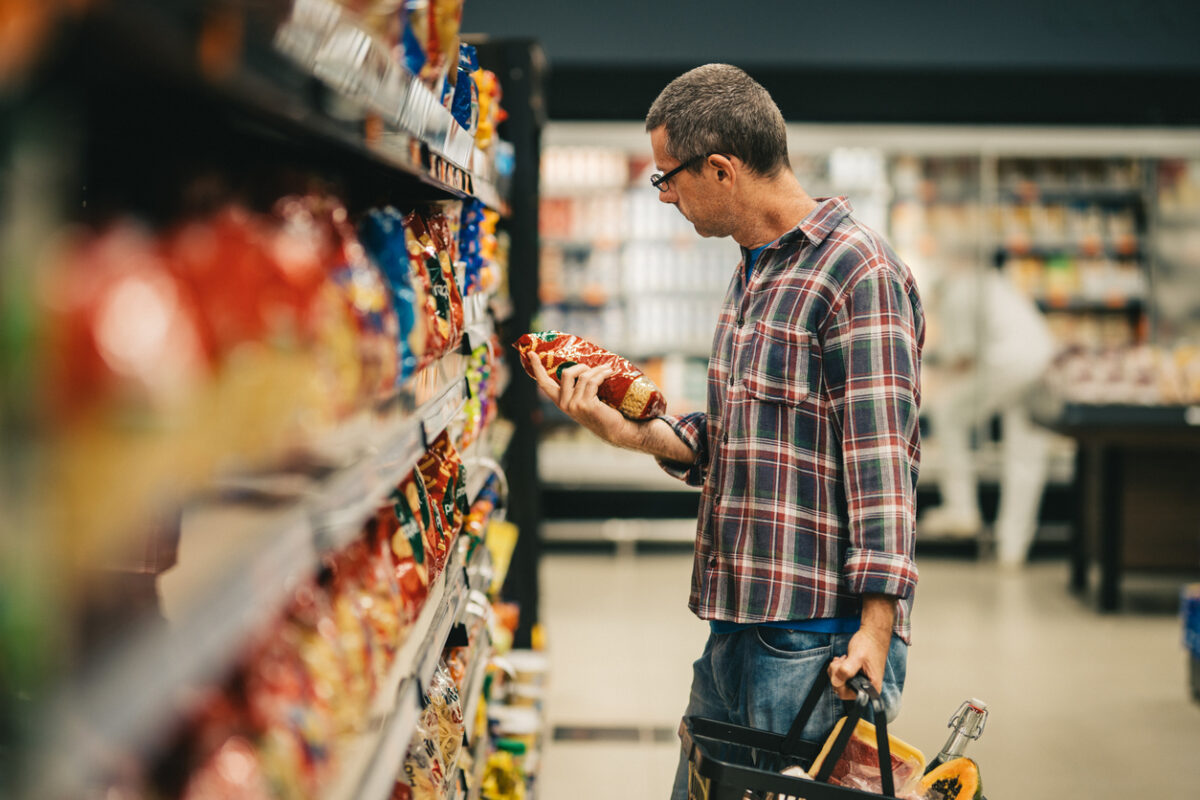Man standing in a supermarket aisle and reading the label on a bag of pasta while grocery shopping