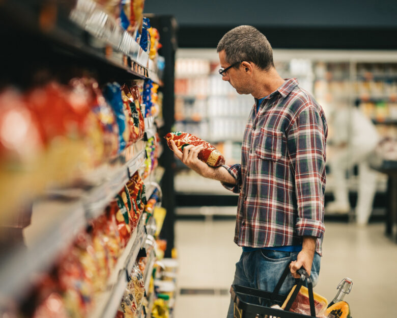 Man standing in a supermarket aisle and reading the label on a bag of pasta while grocery shopping