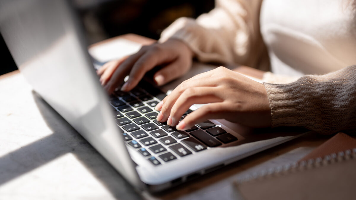 Close-up image of a woman typing on laptop keyboard, working on her laptop computer at a table indoors on a sunny day. businesswoman, student, digital nomad, working remotely
