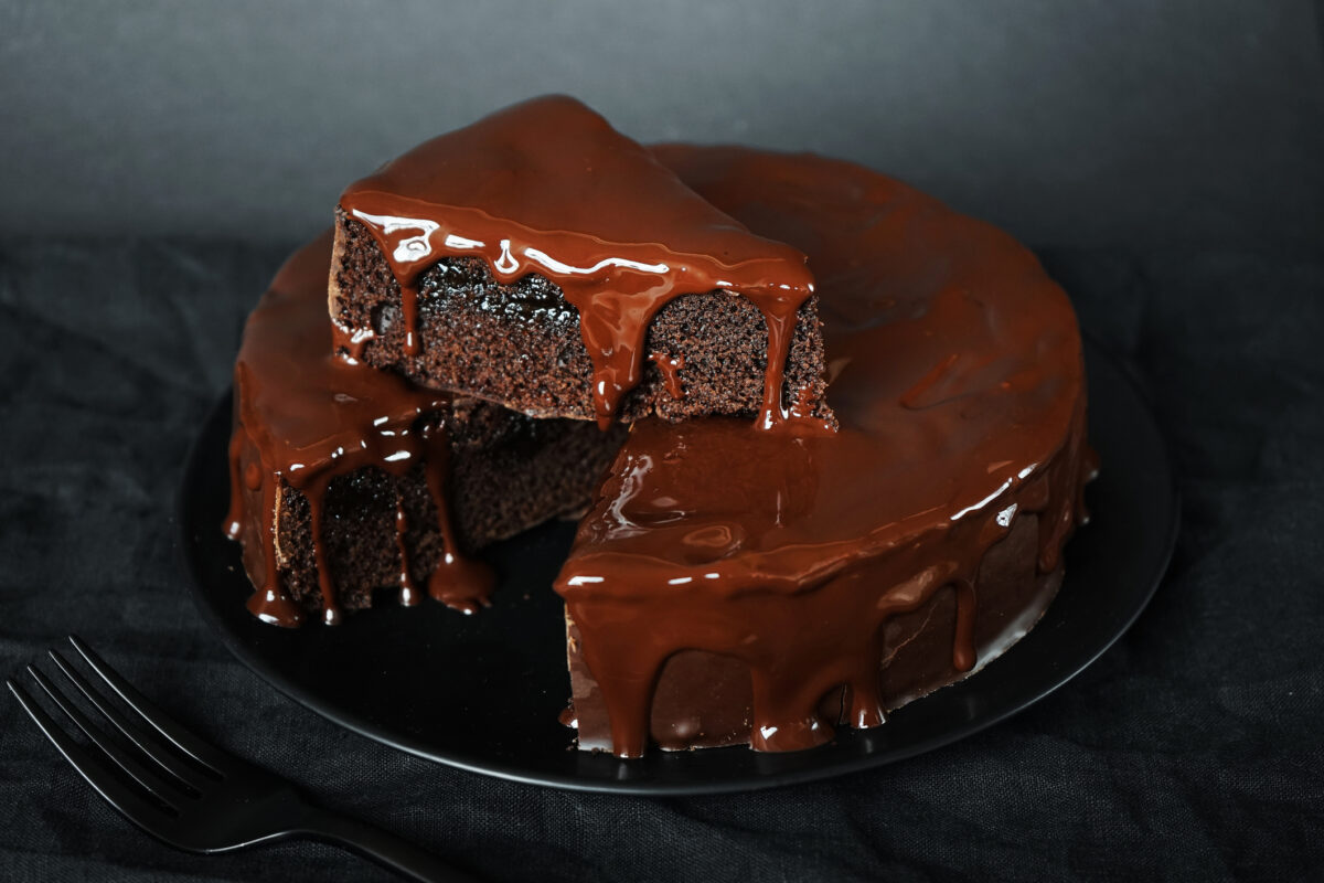 Chocolate cake with chocolate icing on a black plate next to a fork on a dark background