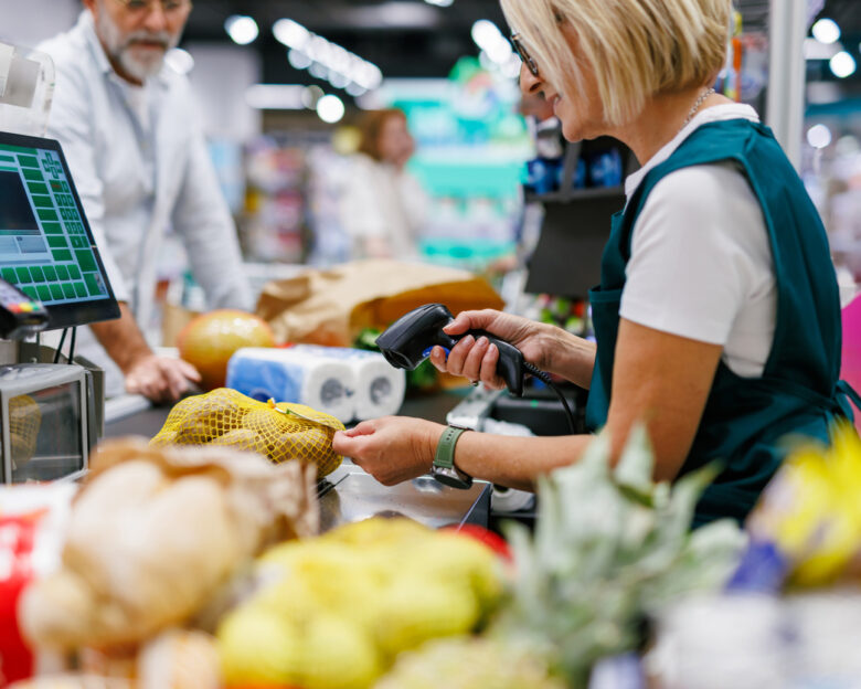 Supermarket cashier scanning groceries at the checkout with barcode reader while customer is waiting, cashier and clients are not recognizable