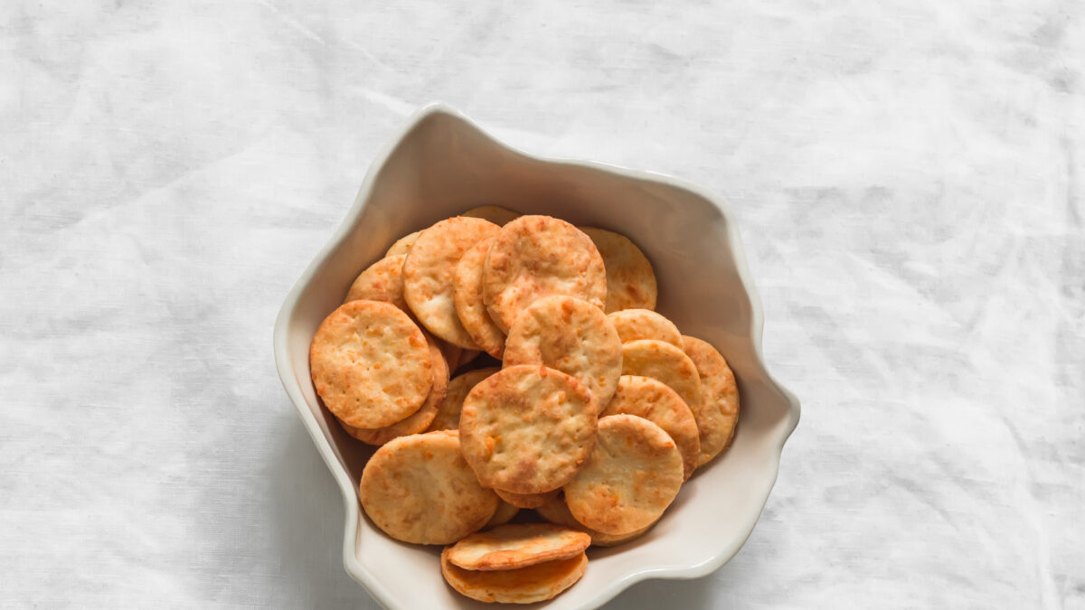Cheddar cheese cracker in a ceramic bowl on a light background, top view