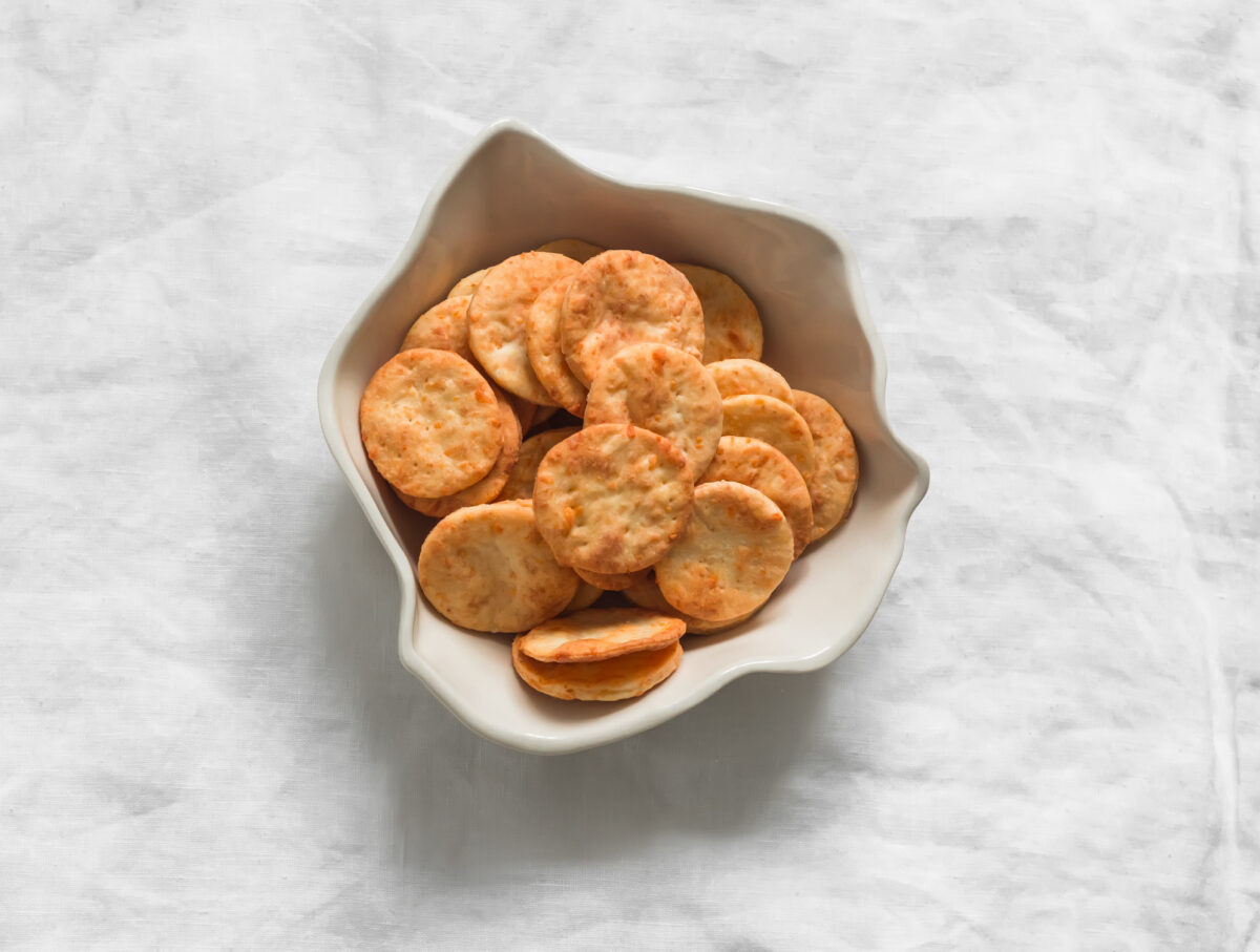 Cheddar cheese cracker in a ceramic bowl on a light background, top view