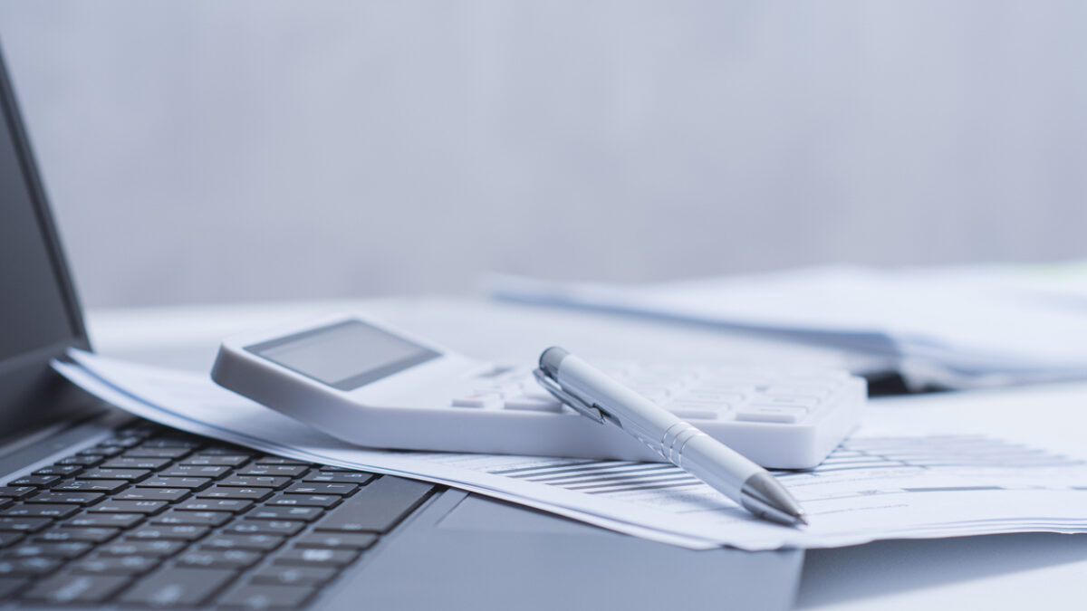 Calculator and pen placed on a white office desk with financial documents and laptop. Clean modern workspace concept for accounting, finance, budgeting and business analysis