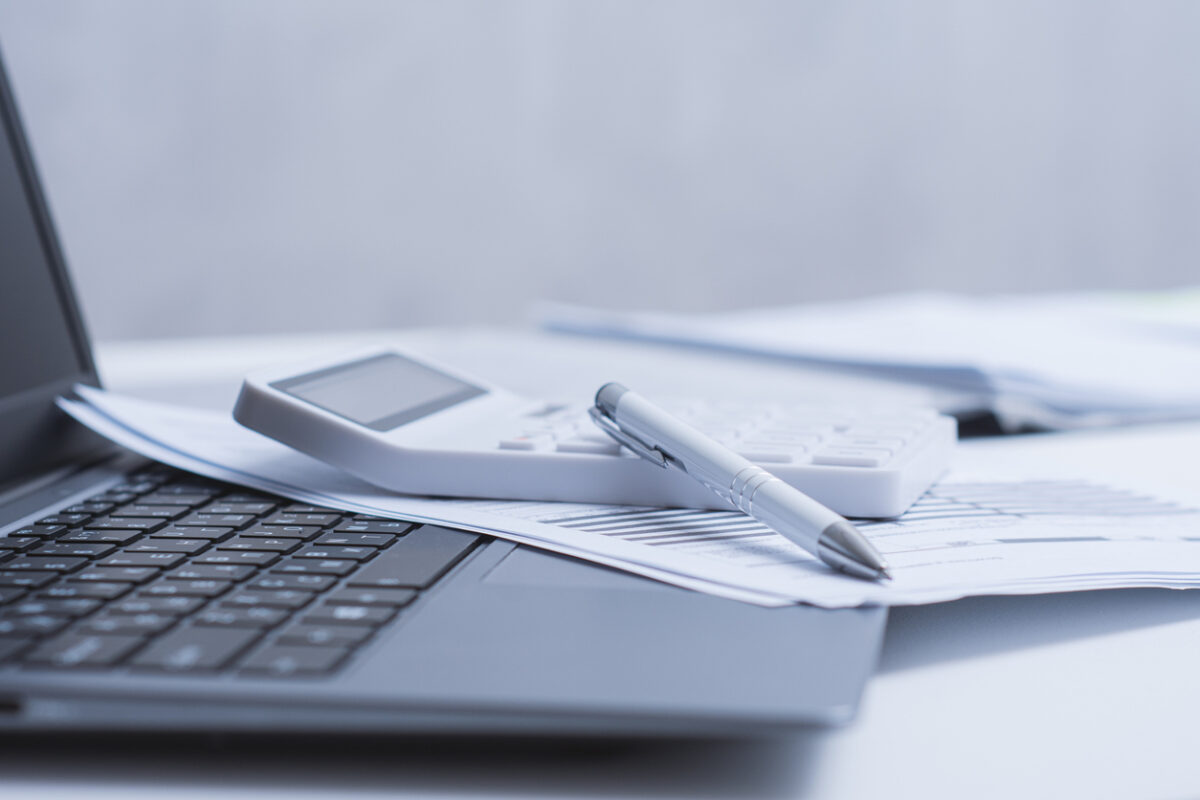 Calculator and pen placed on a white office desk with financial documents and laptop. Clean modern workspace concept for accounting, finance, budgeting and business analysis