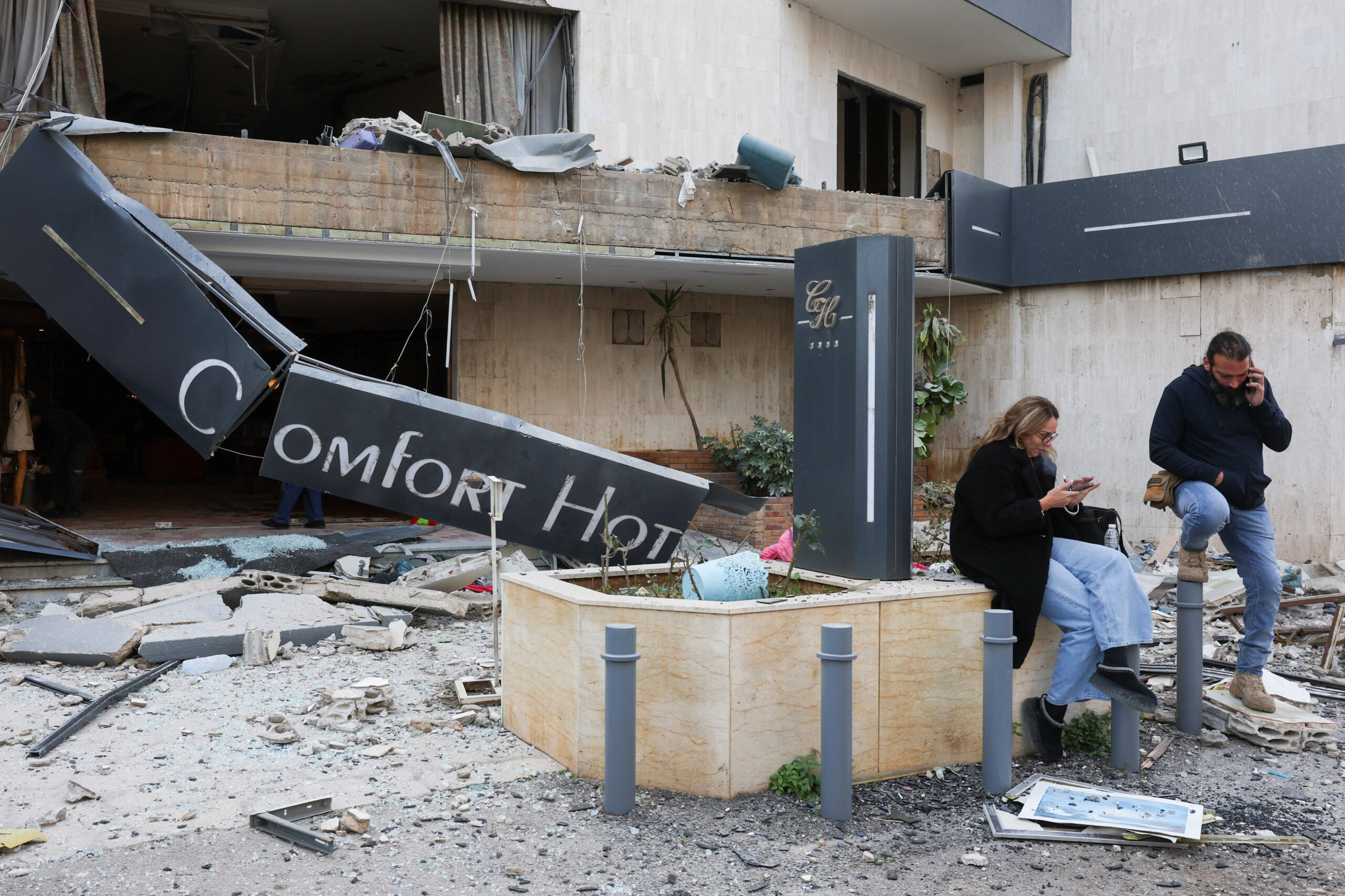 People use their phones next to a damaged building in the aftermath of an Israeli strike, following an escalation between Hezbollah and Israel amid the U.S.-Israeli conflict with Iran, in Hazmieh, Lebanon, March 4, 2026. REUTERS