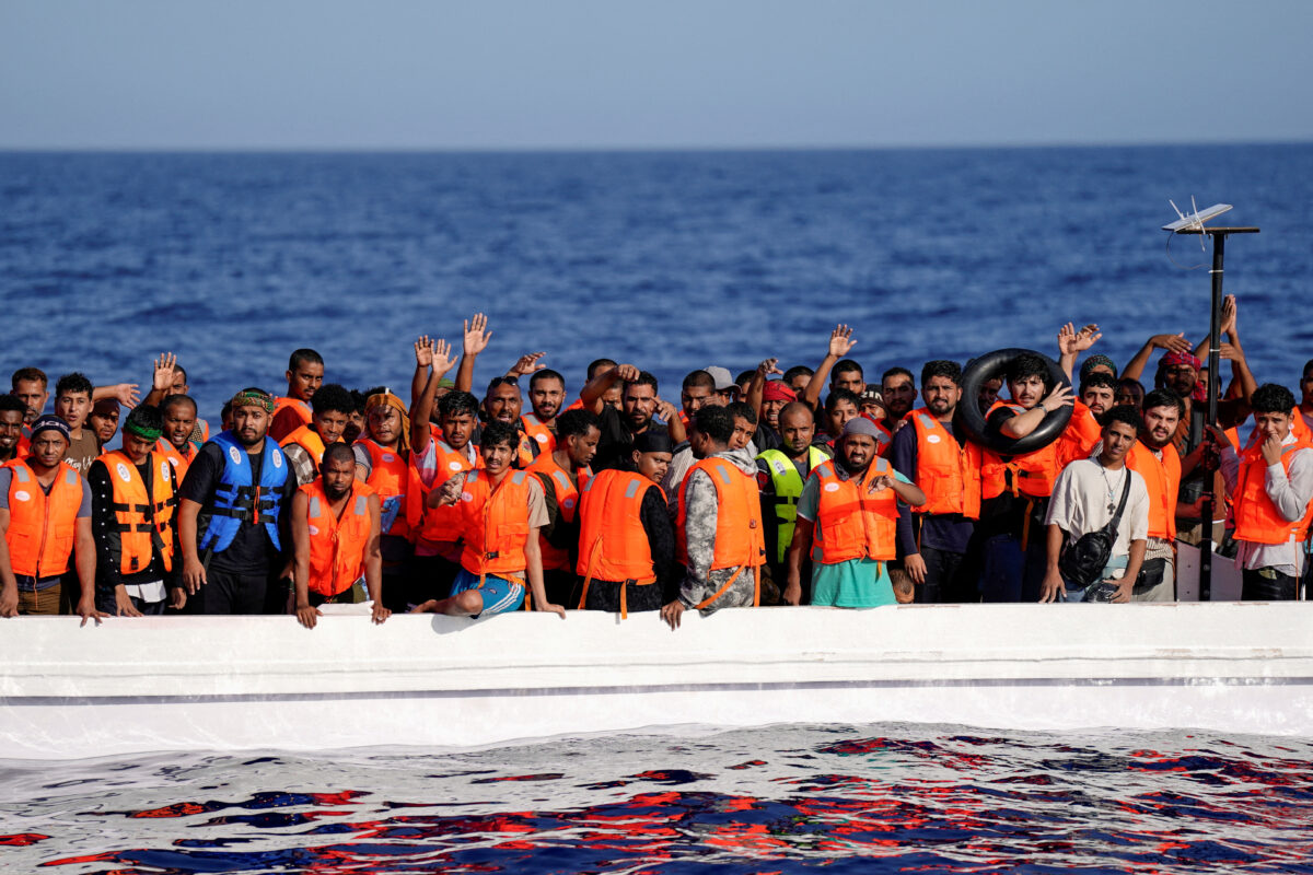 FILE PHOTO: Migrants standing on a fiberglass boat wave at NGO Open Arms rescue boat "Astral" as they assist them in international waters south of Lampedusa, in the Mediterranean Sea, July 24, 2025. REUTERS/Ana Beltran/File Photo