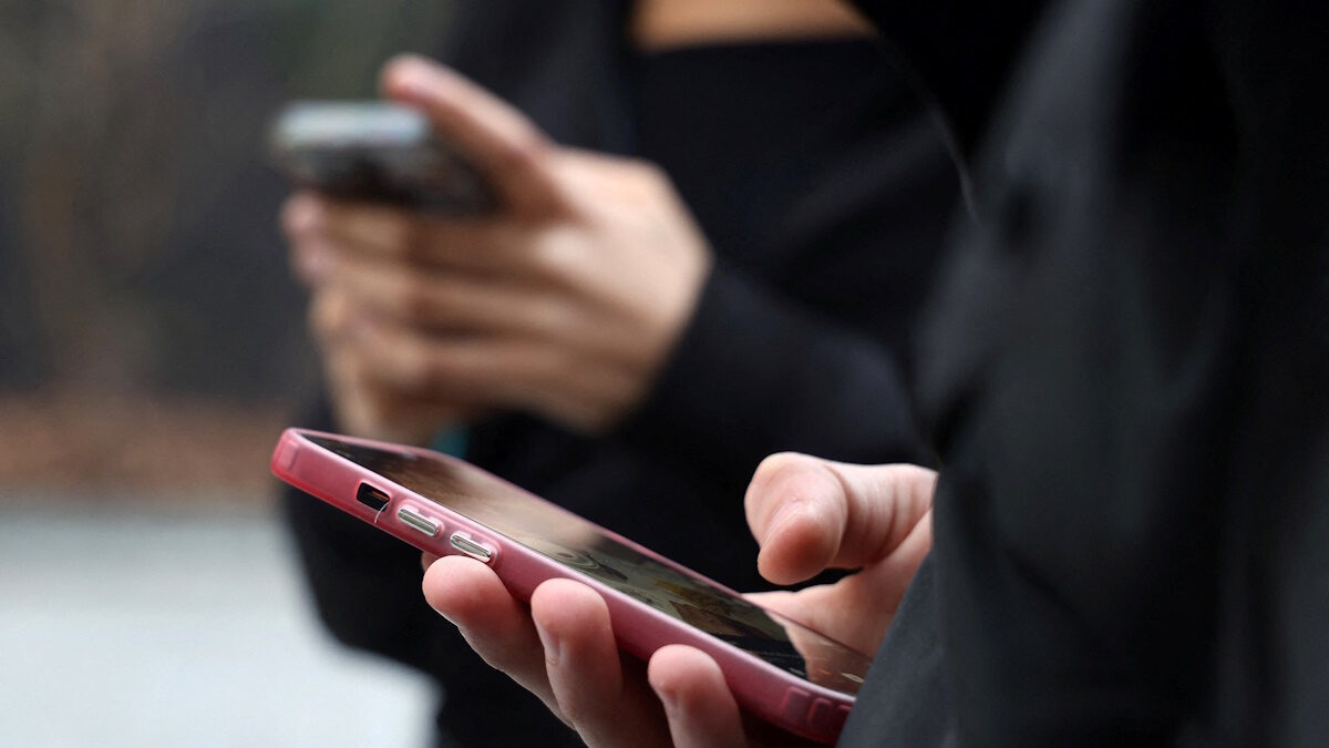 Teenagers look at their mobile phone screens during an interview with Reuters about the bill aimed at banning the use of social networks for those under 15 and mobile phones in high schools from the start of the 2026 school year, in Paris, France, February 20, 2026. REUTERS/Manuel Ausloos