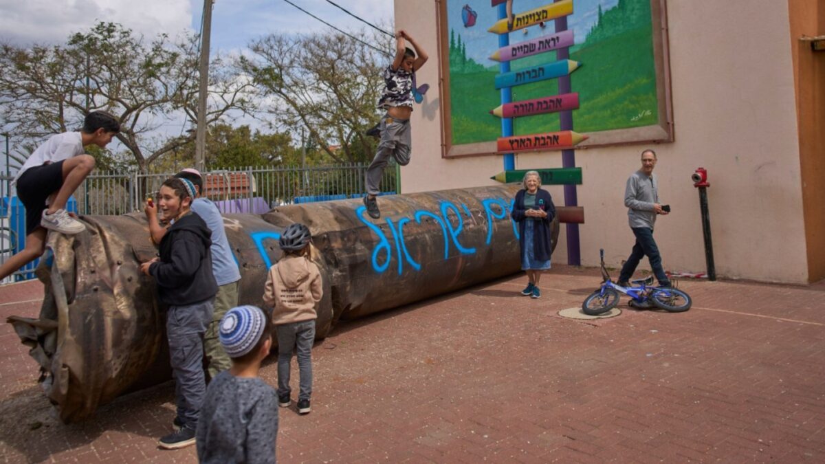 Children play beside a fragment of an Iranian ballistic missile that landed in a schoolyard in the Israeli settlement of Peduel in the West Bank Monday, March 23, 2026. (AP Photo/Ohad Zwigenberg)