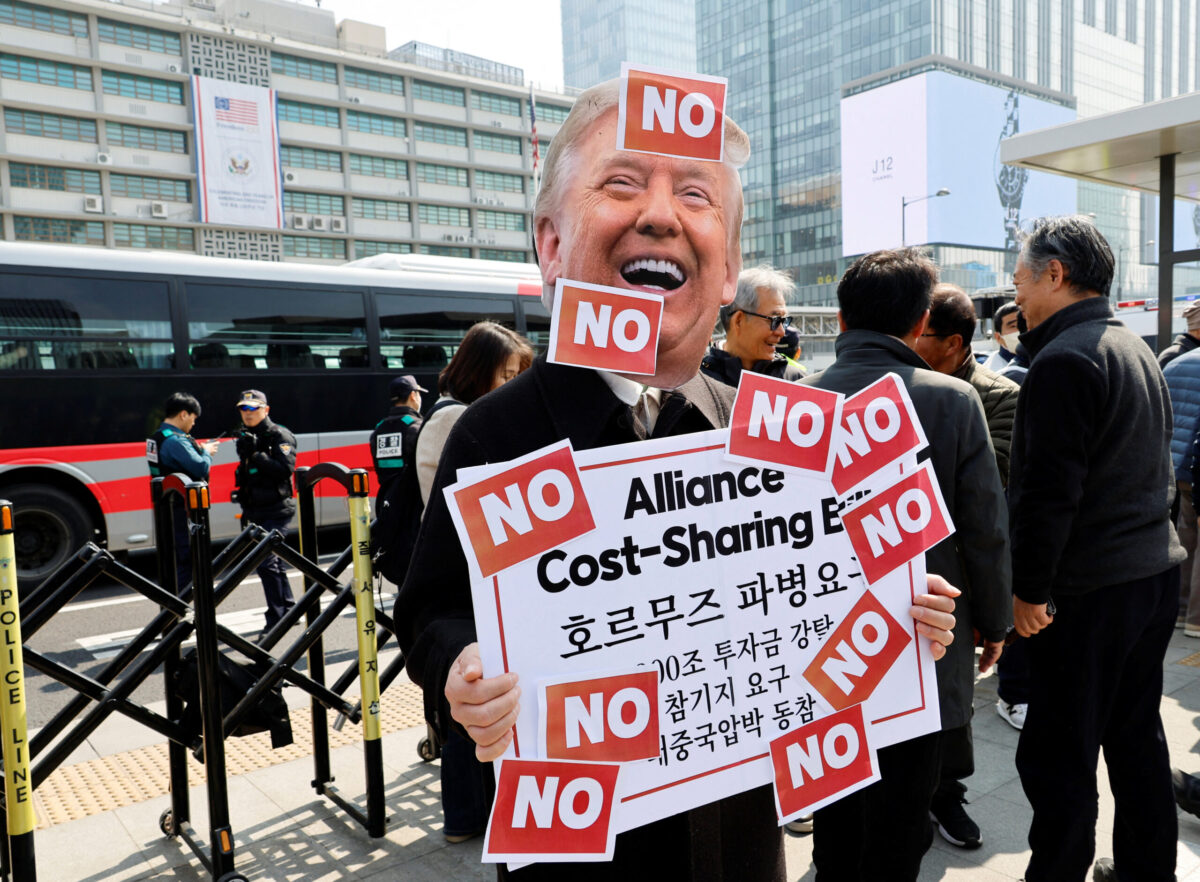 Activists hold a rally against the U.S. demand for South Korea to deploy troops to the Strait of Hormuz, in Seoul An activist wearing a cutout mask depicting U.S. President Donald Trump holds a placard covered with